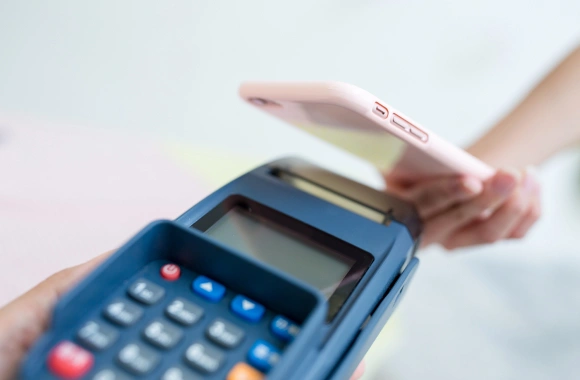 Hand holding credit card over blue payment terminal for transaction processing.