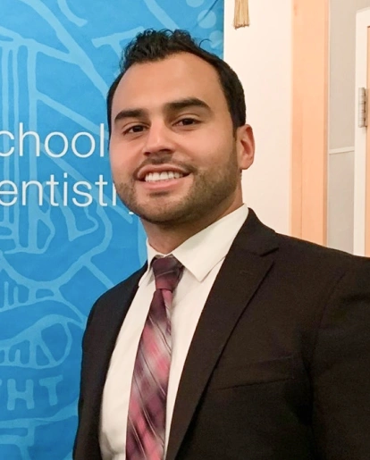 Professional man in business suit smiling at dental office with blue branded backdrop