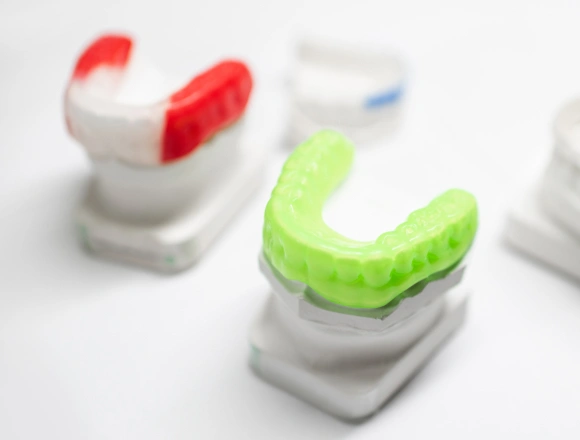 Clear aligners in red, green, and white displayed on white dental models showing orthodontic treatment options.