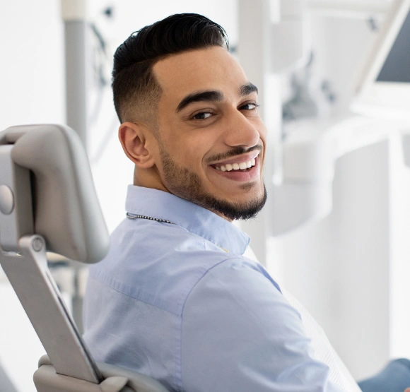 Young man in light blue shirt smiling at dental chair in modern clinic setting.