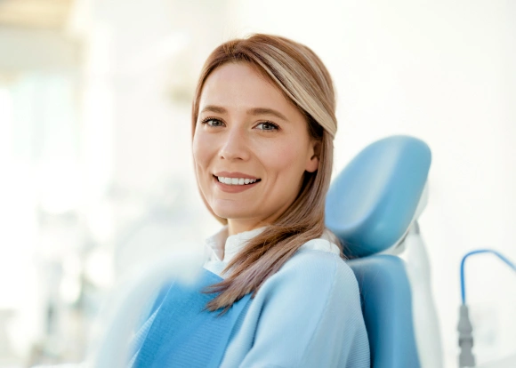 Smiling dental professional in blue scrubs sitting in modern dental office chair.