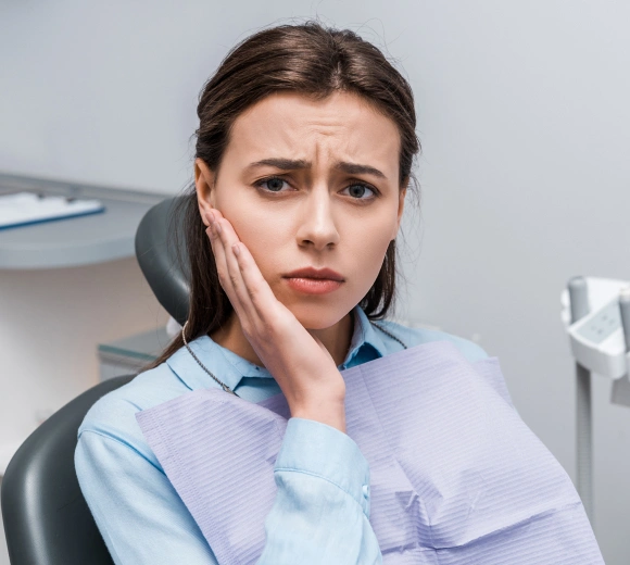 Woman in dental office touching her cheek in discomfort, seated in treatment chair.