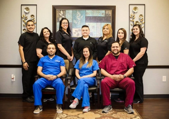 Dental team of approximately 13 staff members posing together in professional uniforms in clinical office setting.