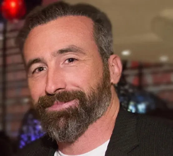 Professional man with beard in dark suit at indoor event venue.
