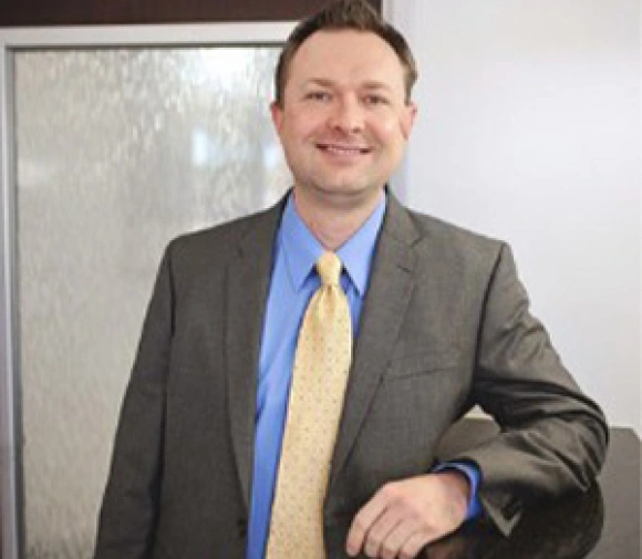 Professional man in gray blazer and yellow tie smiling in office setting.