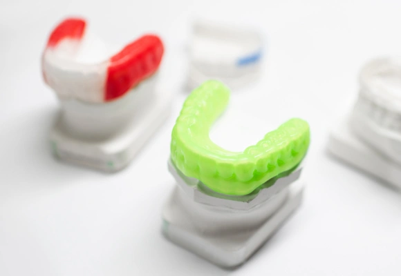 Colorful orthodontic retainers and aligners displayed on white stands, showing dental treatment options.