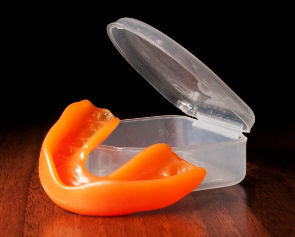Clear plastic retainer case with orange retainer inside, displayed on wooden surface.