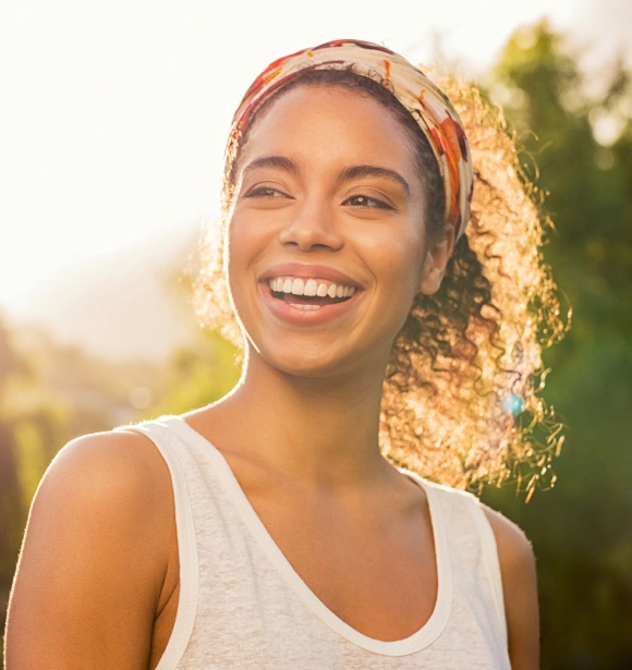Smiling young woman wearing headband outdoors in natural sunlight, displaying healthy teeth and bright expression.