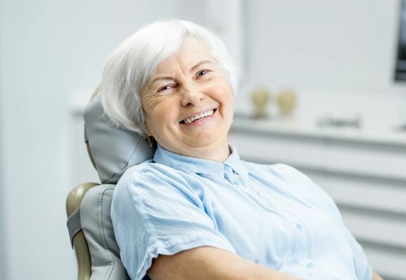 Senior woman smiling in dental chair wearing light blue bib during dental examination.