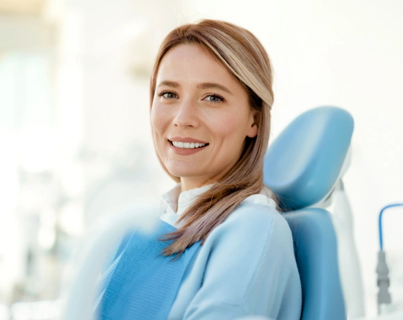 Smiling woman in dental chair wearing blue bib at modern dental office