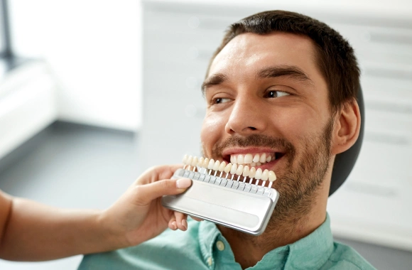 Man holding dental shade guide in dental office, smiling while comparing tooth color samples.