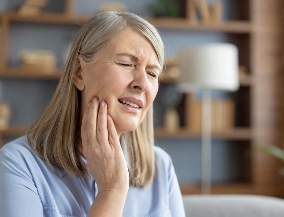 Middle-aged woman holding cheek in pain with shelves in background