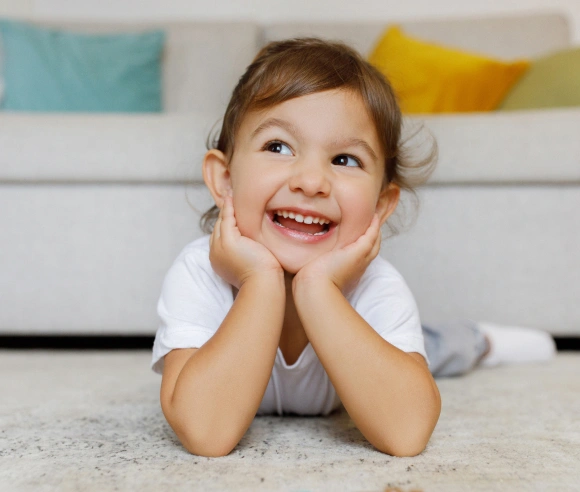 Happy toddler lying on floor smiling, showing healthy teeth in dental office setting.