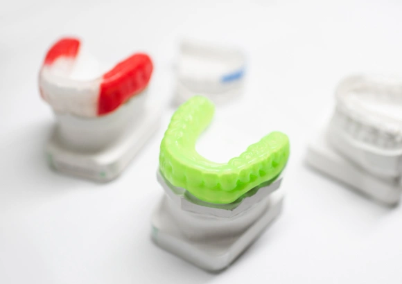 Colorful orthodontic mouthguards and retainers displayed on white stands, showcasing dental appliances.