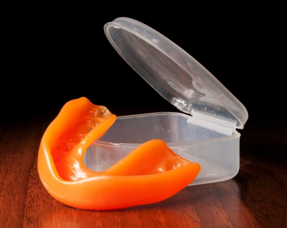 Clear plastic retainer case with orange mouthguard inside on wooden surface