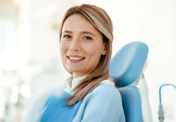 Smiling woman in dental chair wearing blue bib at modern dental office