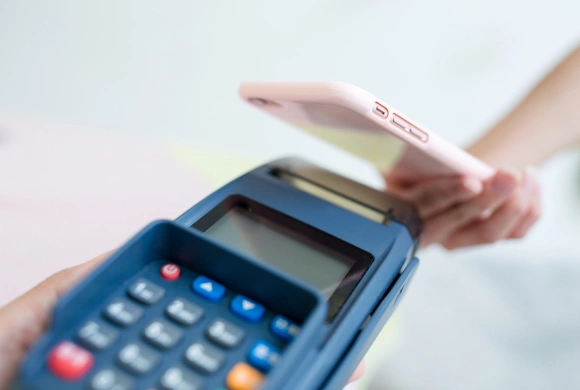 Hand holding credit card over blue payment terminal for contactless transaction.