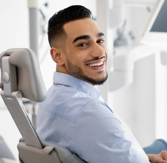 Smiling man in dental chair at modern orthodontic office wearing light blue shirt