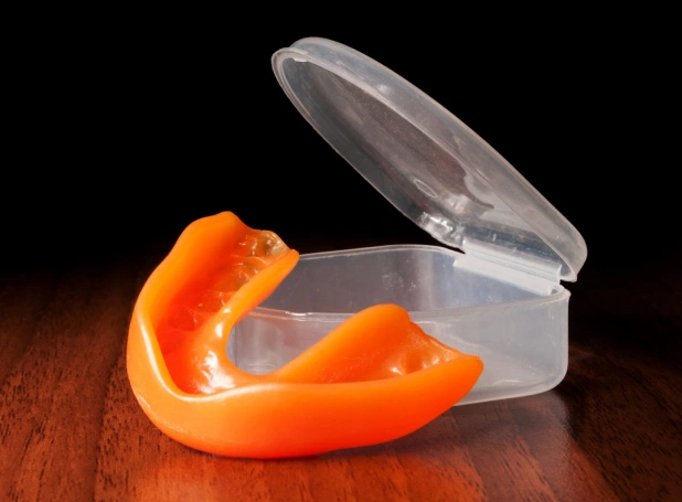 Clear dental retainer container with orange mouthguard on wooden surface.