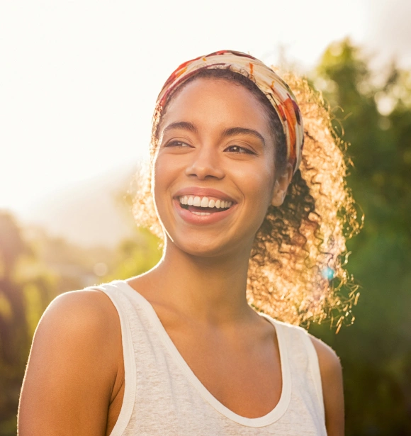 Smiling woman wearing headband outdoors in golden sunlight with trees in background.