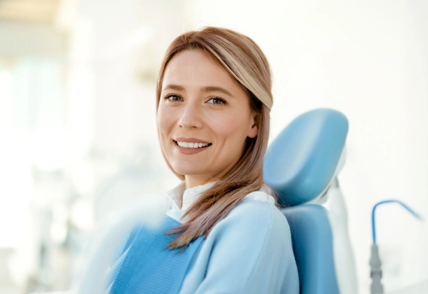 Smiling woman in dental chair at modern dental office, wearing blue bib.