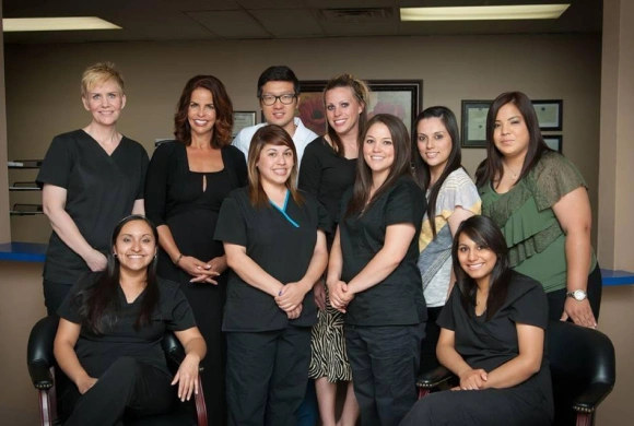 Dental team members posing together in office setting wearing black scrubs and uniforms.