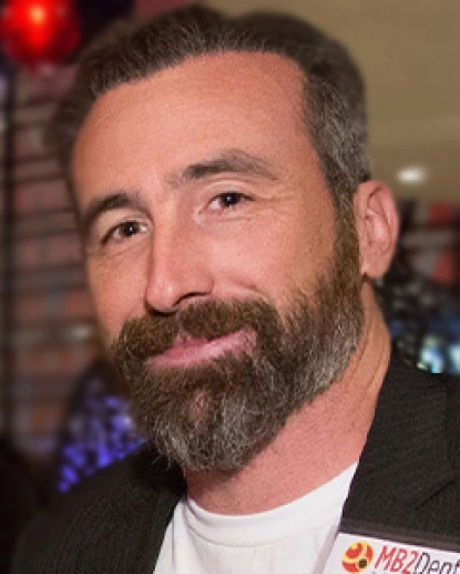 Man with beard smiling at camera in indoor setting with blurred background