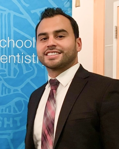 Professional man in business suit and pink tie smiling at dental office reception area.