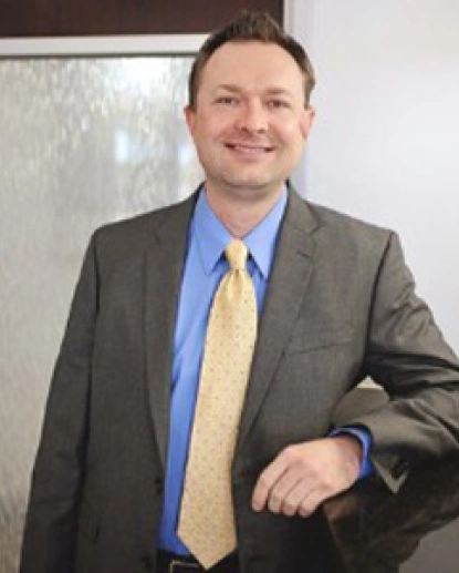 Professional man in business attire smiling at camera in office setting.