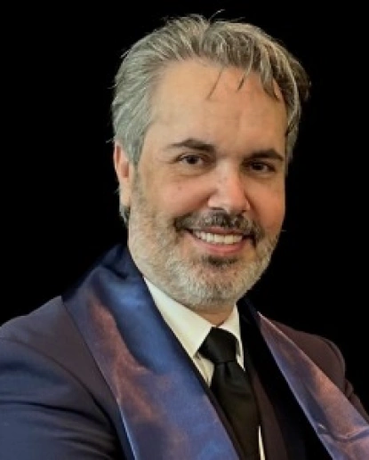 Professional headshot of a man in blue blazer and tie against dark background for dental practice.