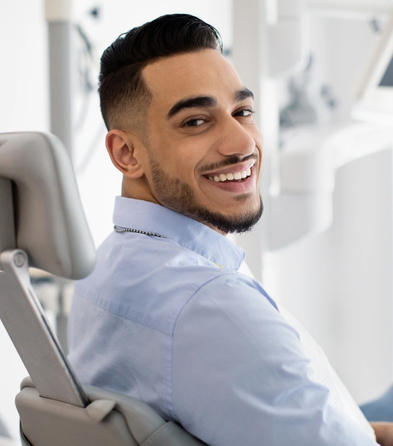 Smiling man in light blue shirt sitting in dental chair at modern clinic