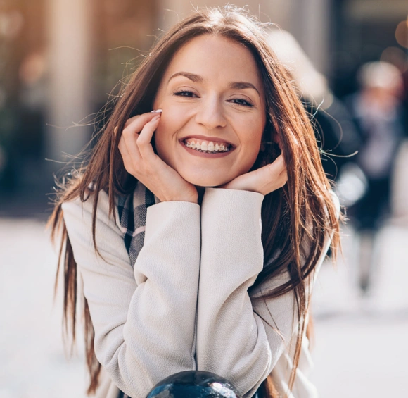 Smiling young woman in white jacket poses outdoors, showcasing healthy teeth and bright smile.