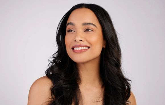 Woman with long dark wavy hair smiling against white background for dental practice.