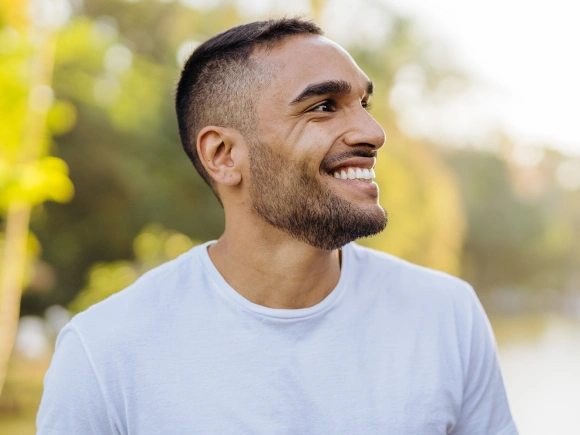 Smiling man in light blue shirt outdoors with blurred green background, dental health portrait.