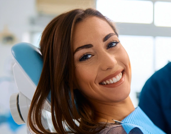 Smiling woman in dental chair at orthodontic office with blue headrest visible.