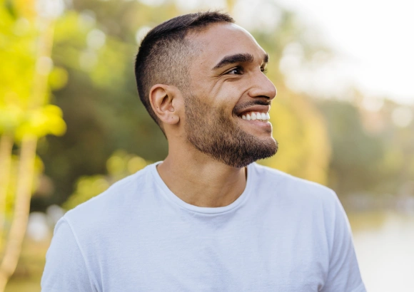 Smiling man in light blue shirt outdoors with blurred green background, dental health portrait.