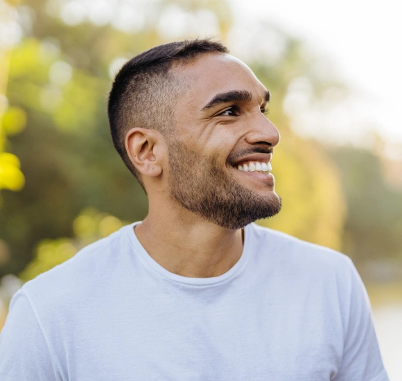 Smiling man in light blue shirt outdoors with blurred green background
