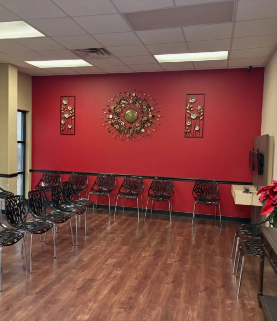 Modern dental waiting room with red walls, decorative wreath, black chairs, and wood flooring.