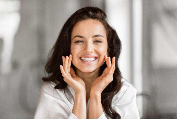 Smiling woman with hands to face in bright dental office setting, promoting dental care.
