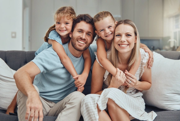 Happy family of four smiling together on couch at home.