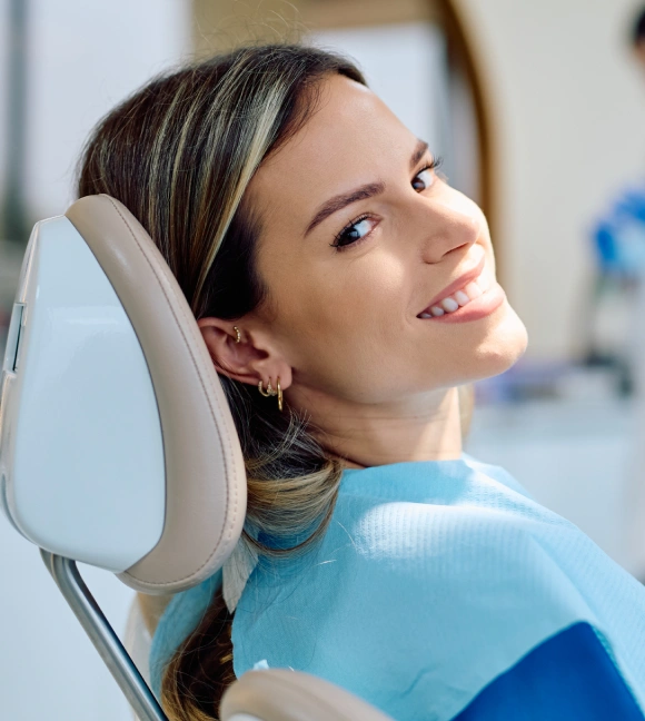 Woman in dental chair wearing blue bib, smiling during orthodontic examination at dental office.