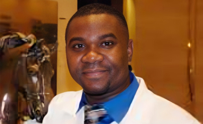 Male dental professional in white coat and blue stethoscope smiling in clinical office setting.
