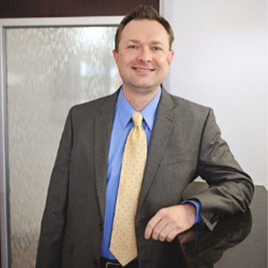 Meet Dr. Nathan Galloway | Professional man in gray blazer and blue shirt smiling in office setting