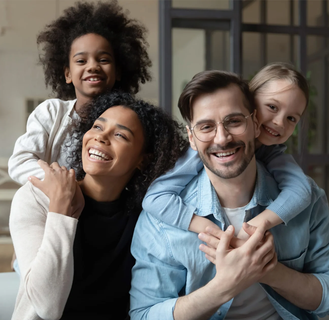 Happy diverse family smiling together in casual indoor setting, representing dental care and wellness.