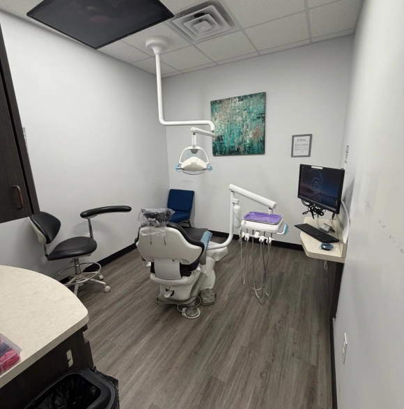 Modern dental treatment room with chair, overhead light, computer monitor, and clinical equipment.