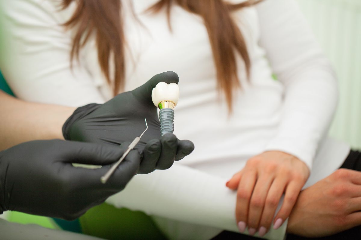 Dentist holding a dental implant model while explaining treatment options to a patient.